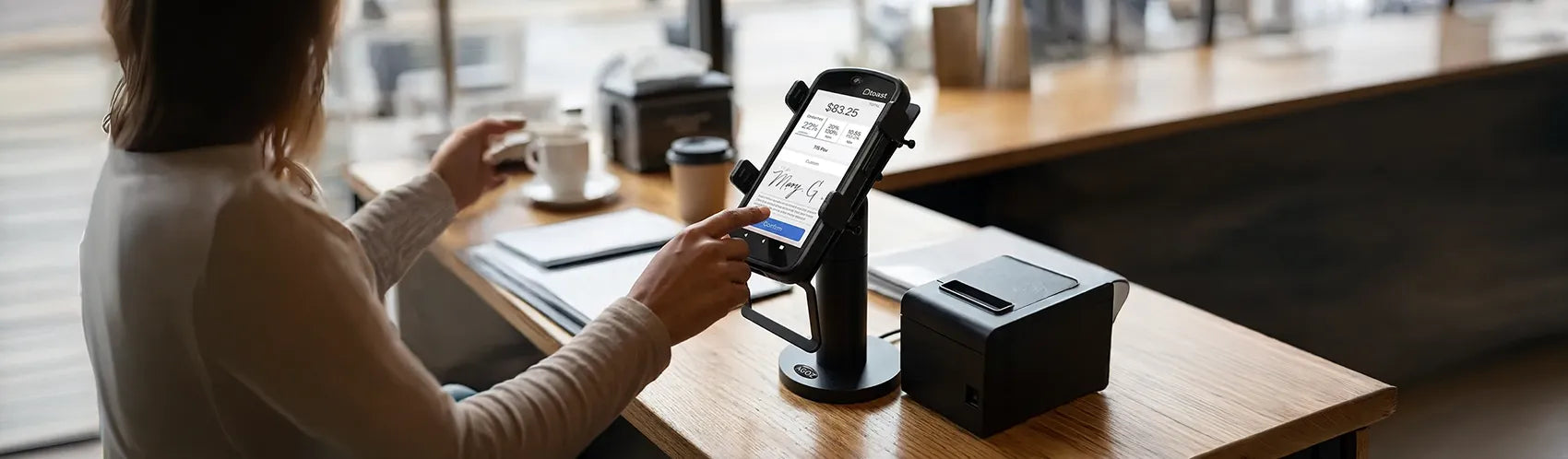 Customer using a mounted Toast Go 2 payment terminal on a checkout counter beside a receipt printer in a retail or café setting.