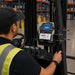 Forklift operator using a mounted SATO mobile printer secured in an AgozTech metal holder for warehouse labeling.