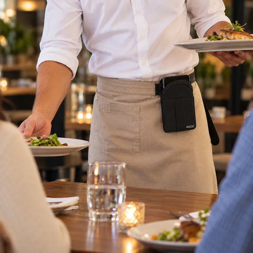 Restaurant server wearing a black Agoz Adyen POS terminal carrying case with metal belt clip while delivering meals to customers.