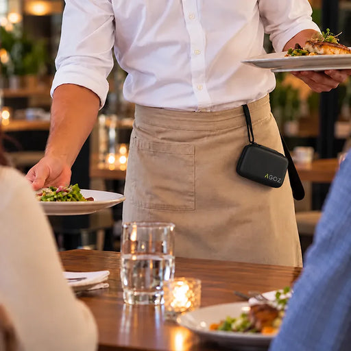 Restaurant server wearing an Agoz Clover Go carrying case attached to an apron while serving meals, demonstrating hands-free storage during table service.