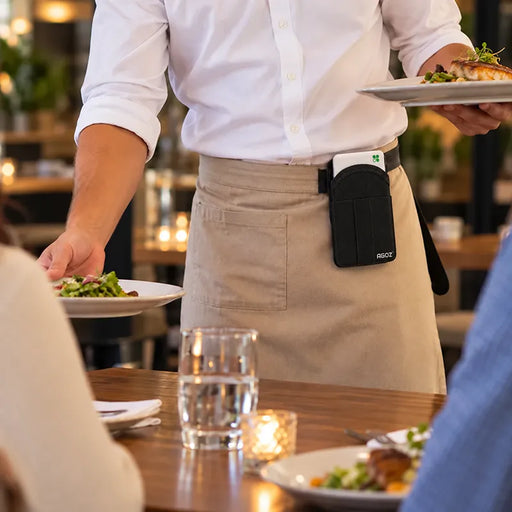 Restaurant server wearing an Agoz Clover POS holster attached to a beige apron while serving meals, demonstrating hands-free payment terminal storage during table service.