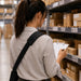 Worker wearing shoulder sling holster while reviewing a clipboard and checking inventory on warehouse shelving.