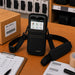 Black Newland shoulder sling holster on a warehouse workstation with barcode labels, pick list, and packing supplies.