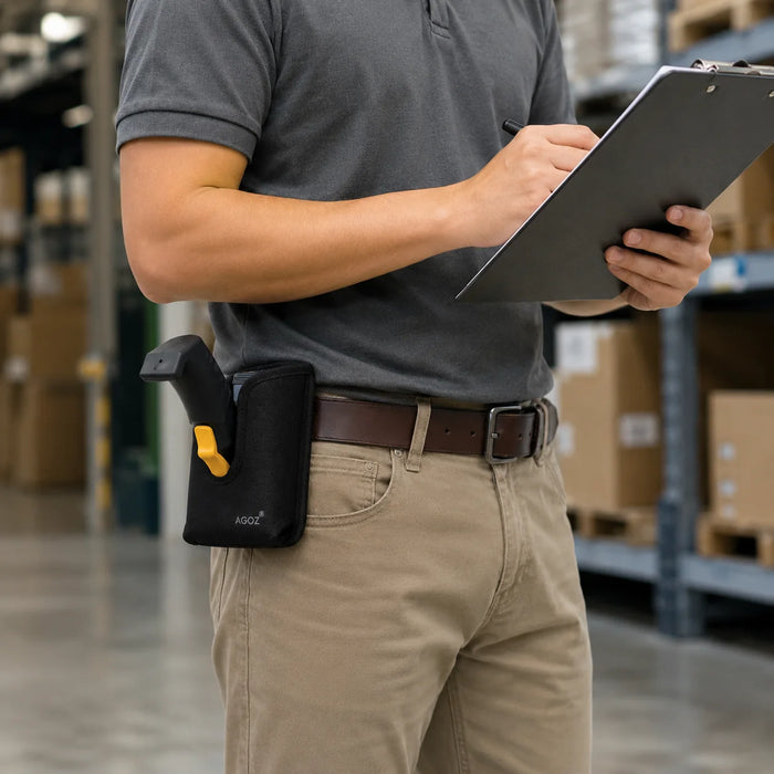 A person in a gray polo shirt and khaki pants stands in a warehouse holding a clipboard, with a black Bluebird scanner holster containing a grip attached at the waist.