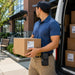 Delivery driver holding a package with both hands beside a delivery van, wearing a compact black AGOZ belt case on his front hip.