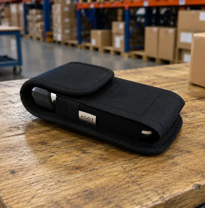 Black AGOZ Zebra scanner case holding a handheld device on a wooden warehouse worktable, with storage racks and boxes in the background.