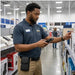 Retail worker wearing an AgozTech rugged Zebra handheld case with belt clip while scanning shelf inventory in an electronics store aisle.