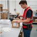 Warehouse worker using a Keyence trigger scanner to scan a shipping box while wearing the black Agoz trigger scanner case on a belt at a packing station.